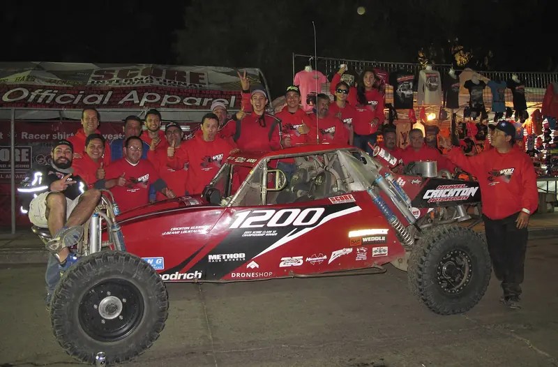 Equipo celebrando junto a su buggy en la meta de la Baja 1000 de 2016, de noche