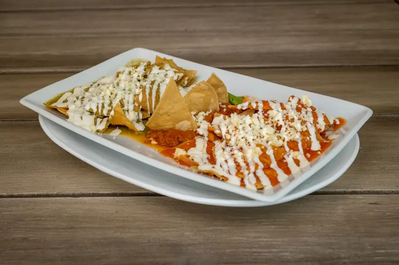 A plate of chilaquiles with red and green salsa, cream and crumbled cheese on a wooden table