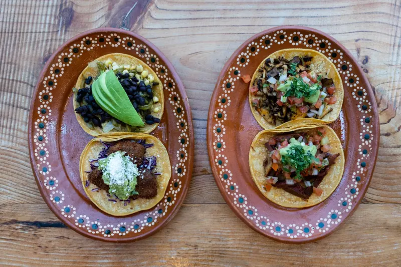Tacos con aguacate y salsa en dos platos de barro sobre una mesa de madera