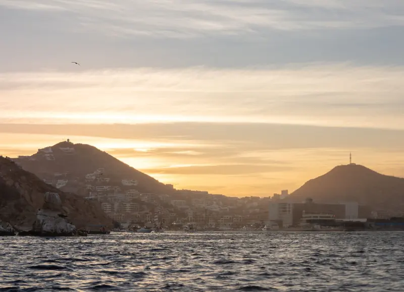 Hills and buildings of Cabo San Lucas at sunset, seen from the water of the bay