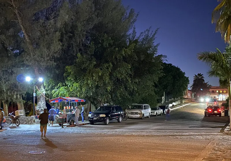 Downtown Todos Santos street at night with lit street lamps, parked cars and people walking