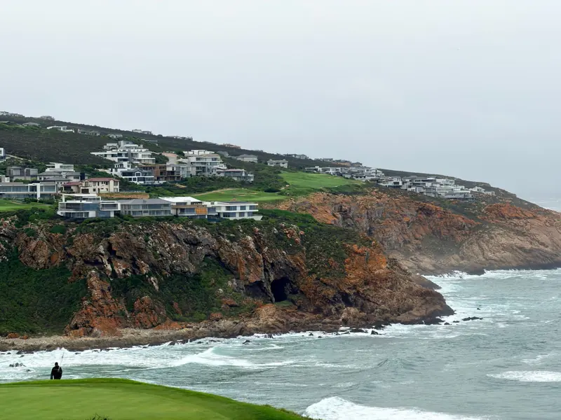 Un campo de golf junto al mar sobre acantilados, con casas a lo largo de la loma