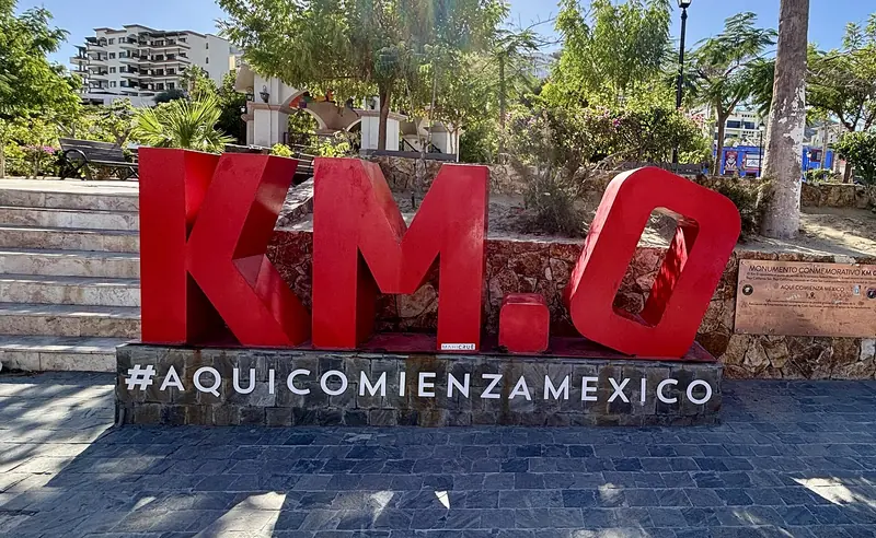 Red Kilometer 0 letters in a shaded plaza in downtown Cabo San Lucas