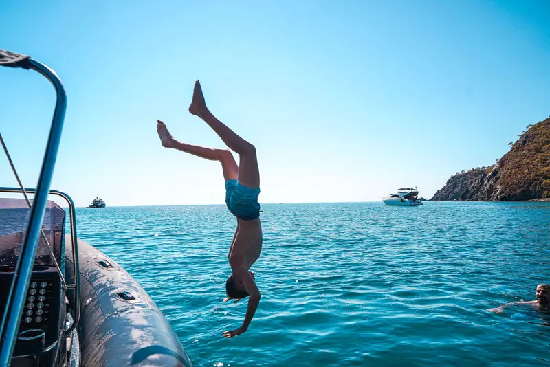 A swimmer diving head first off the side of a boat into clear blue water