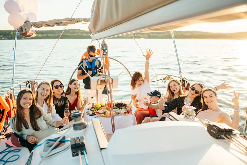 A group of friends laughing and raising their arms on the deck of a boat in the afternoon sun