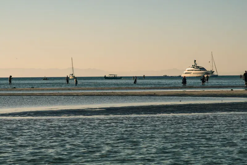 Sunset over the bay at La Paz with people wading on a sandbar and a yacht at anchor