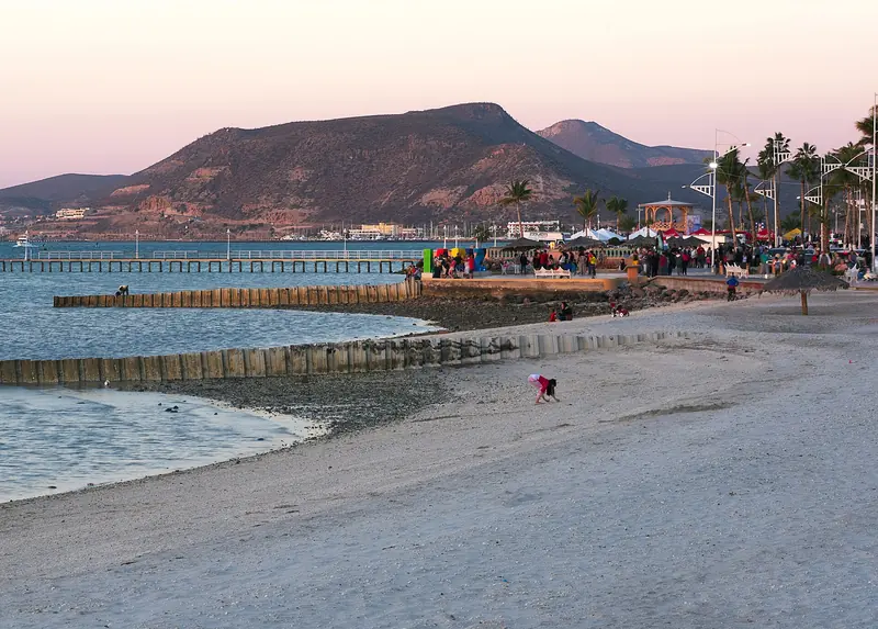 The La Paz malecón at sunset with crowds near the kiosk and a hill behind
