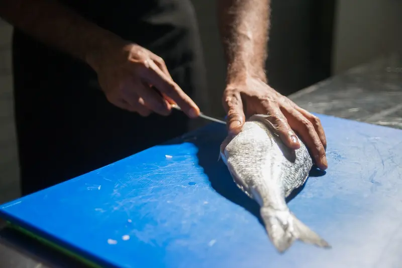 Persona limpiando un pescado entero con cuchillo sobre una tabla azul