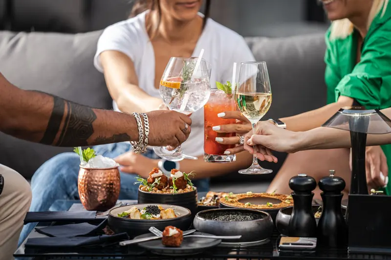 Colegas brindando con cocteles sobre una mesa con comida en una reunión al aire libre