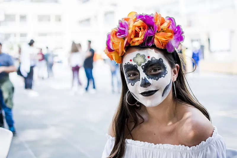 Joven con maquillaje de catrina y corona de flores naranjas y moradas en un festival en México