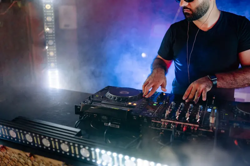 DJ con audífonos mezclando en una consola con luces azules y humo