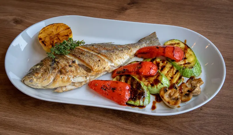 A grilled fish with roasted peppers and vegetables on a white plate