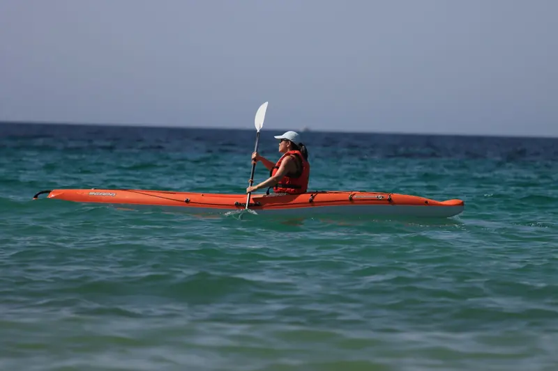 A paddler in a life vest in an orange sea kayak on open water