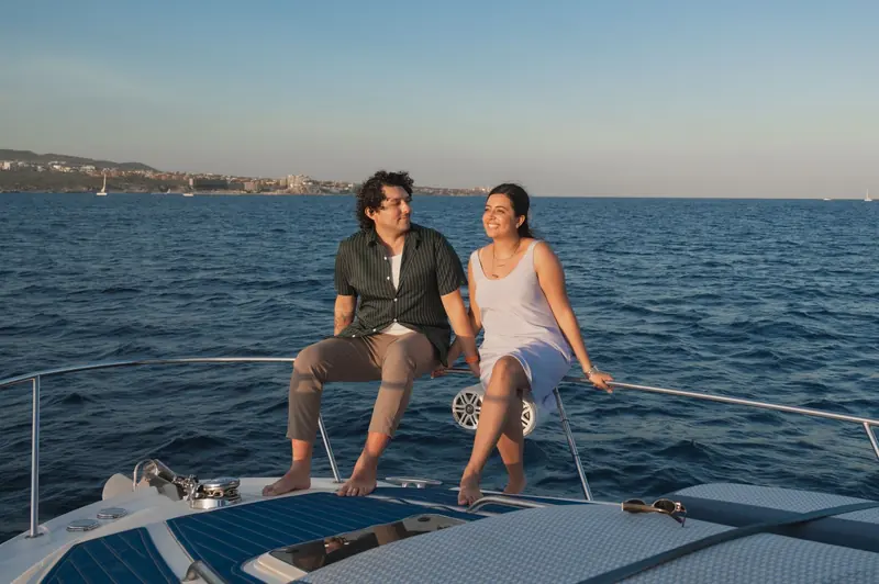 Una pareja sentada en la proa de un yate con el mar abierto detrás