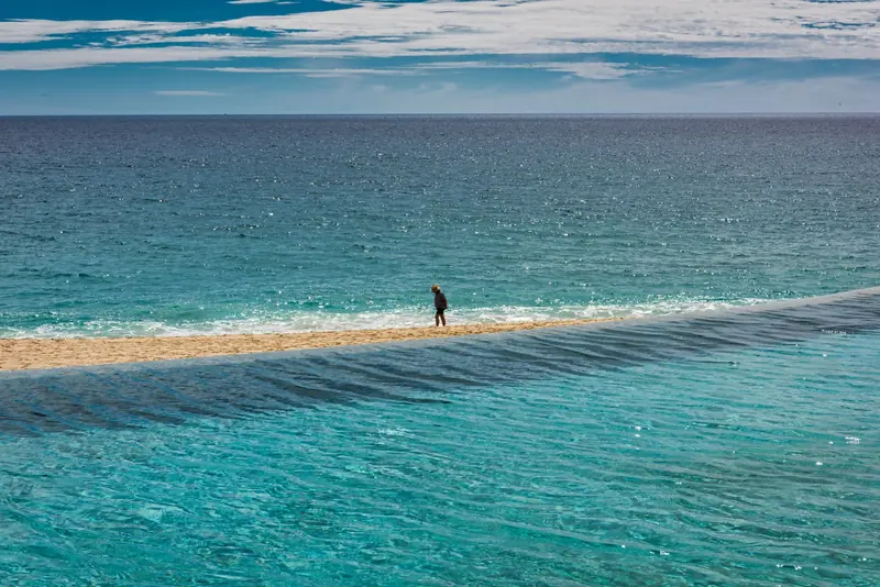 A person walking along the shoreline of a beach in San José del Cabo under a blue sky