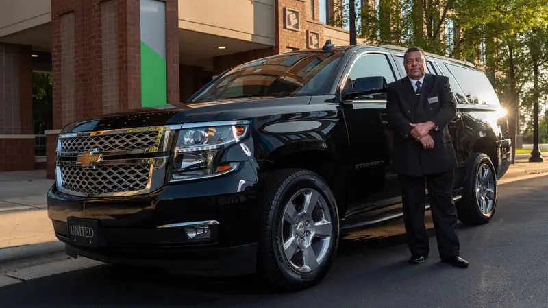 Driver in a dark suit standing beside a black SUV at a hotel entrance