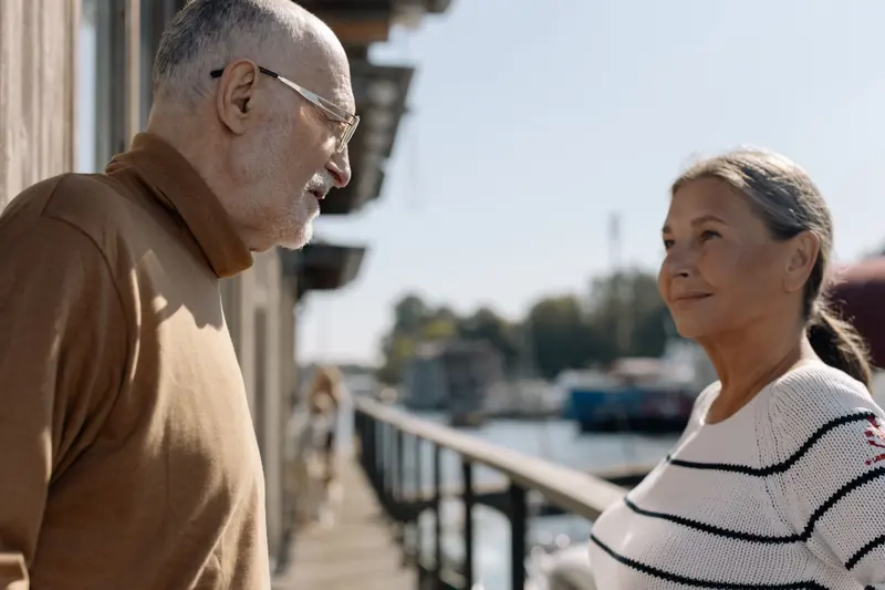 An older couple smiling together on a waterfront walkway on a sunny day