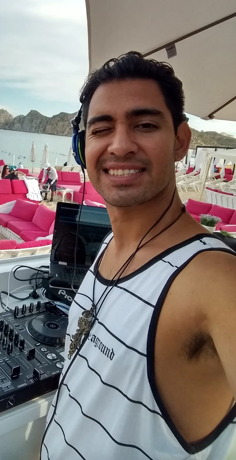 DJ Basneit at his booth in a Cabo beach club, with the Land's End rocks behind him