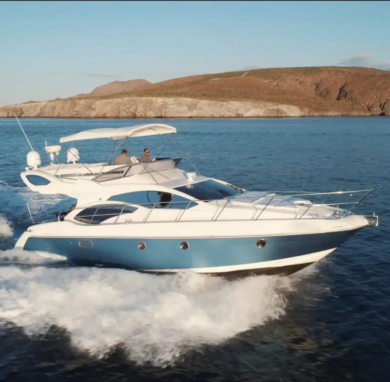 The Azimut 45 Flybridge running across the bay with two people at the flybridge helm and the coast behind