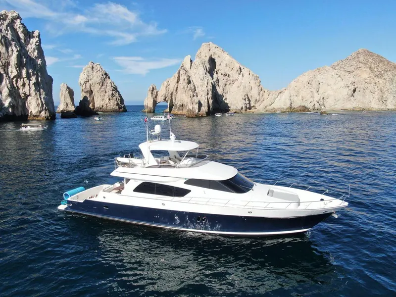 The McKinna 70 luxury motor yacht on calm blue water in front of the Arch and the rock pinnacles of Land's End