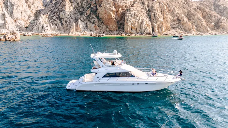 The Sea Ray 55 flybridge yacht cruising past the granite cliffs of Land's End with guests on the bow and the flybridge