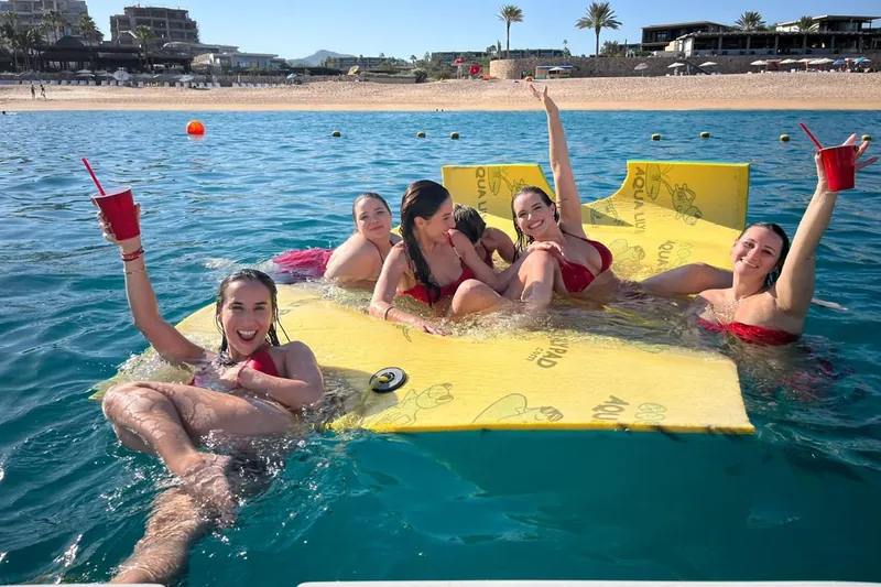 Six friends in red swimsuits on the Sea Ray 55's floating mat off Médano Beach, drinks in hand